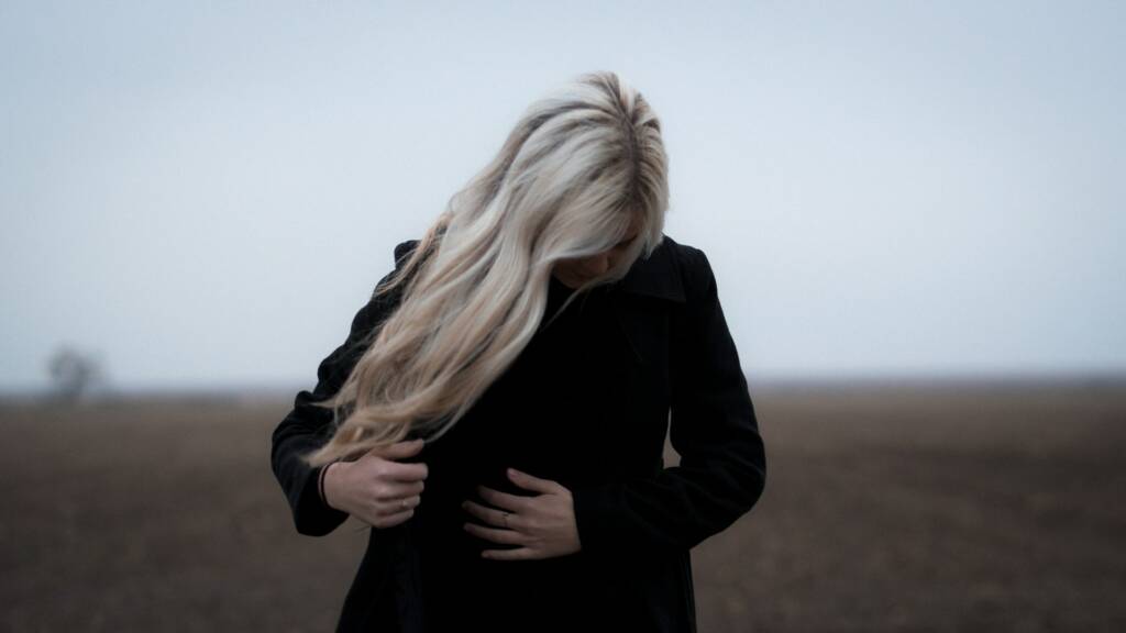 Une femme tête baissée remet son manteau au milieu d'un champs